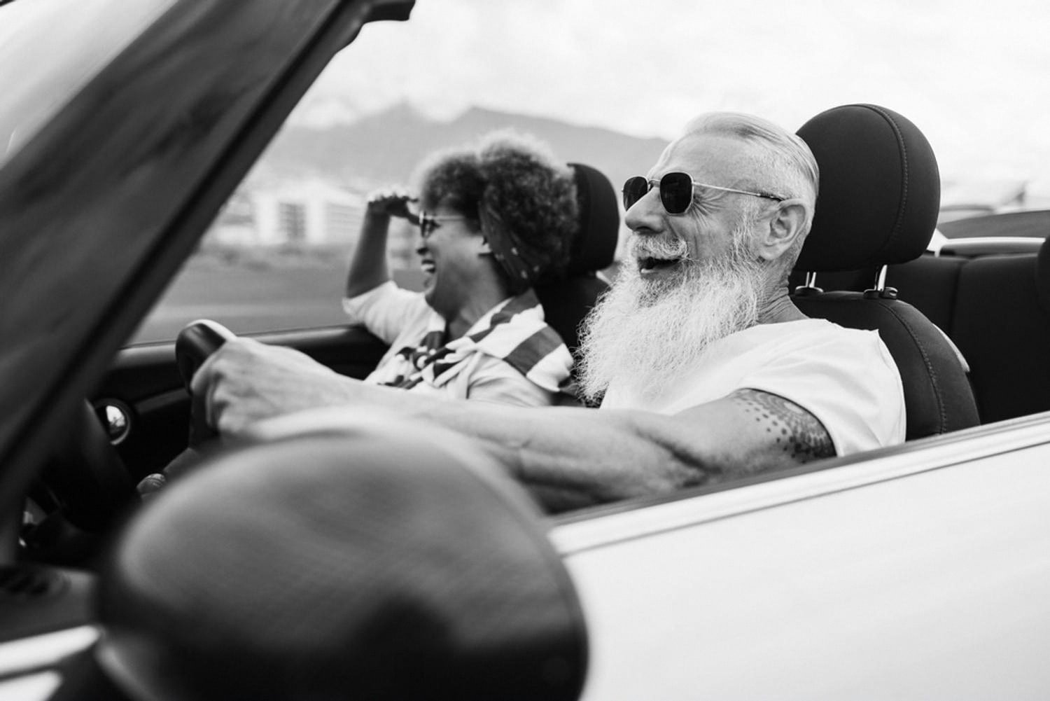 Older couple driving a convertible along an open Australian road with mountains in the background
